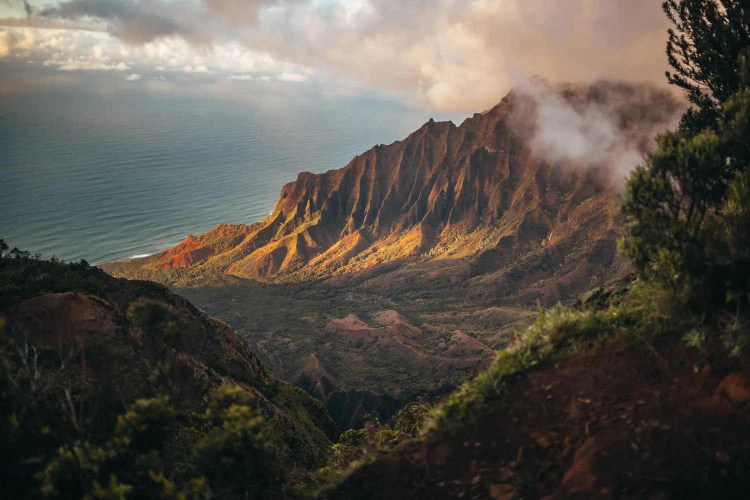 Warm light on the fluted ridge above Kalalau Valley, with a wisp of cloud lifting off the peak and the ocean stretching out beyond